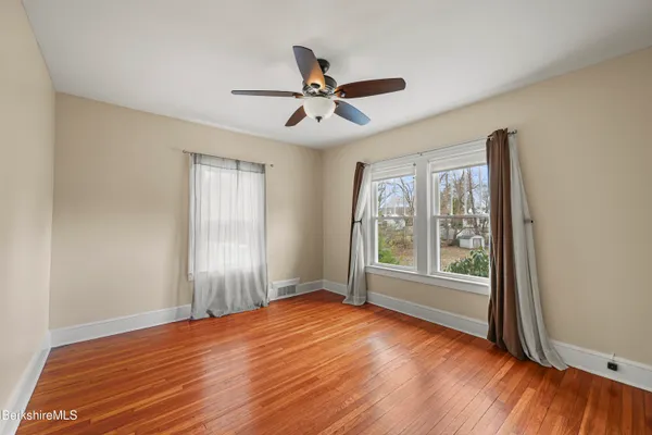 an empty room with wooden floor fan and windows