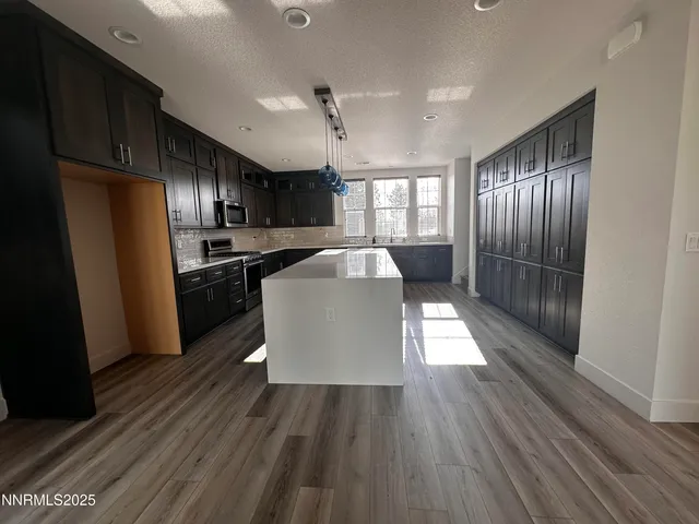 a kitchen with stainless steel appliances granite countertop a refrigerator a sink dishwasher a stove and white countertops with wooden floor