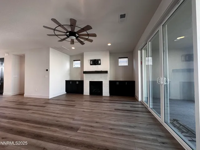 a view of a livingroom with a fireplace a ceiling fan a kitchen space with wooden floor