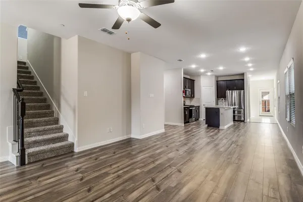 a view of an empty room with wooden floor kitchen view and a window