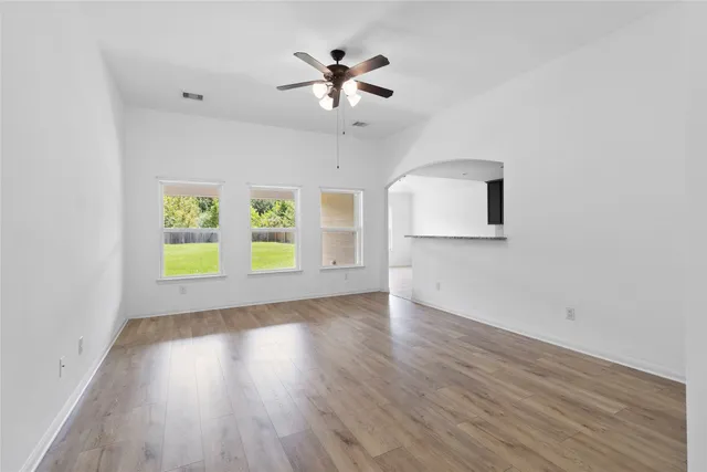 an empty room with wooden floor chandelier fan and windows