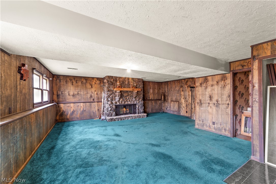 18763 Sharon Road Chagrin Falls, OH 44023 - Photo 24 of 37 Family room featuring a textured ceiling, a fireplace, wood walls, and dark colored carpet