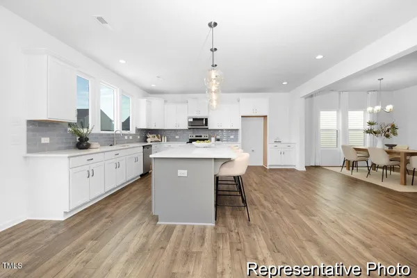a kitchen with stainless steel appliances kitchen island granite countertop a stove a sink a refrigerator and white cabinets with wooden floor