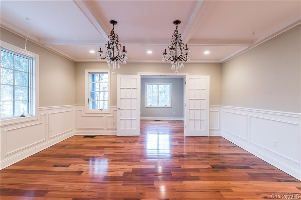 1 Elizabeth Road New Rochelle, NY 10804 - Photo 10 of 23 Unfurnished dining area with a chandelier, beamed ceiling, a decorative wall, wood finished floors, and a wainscoted wall
