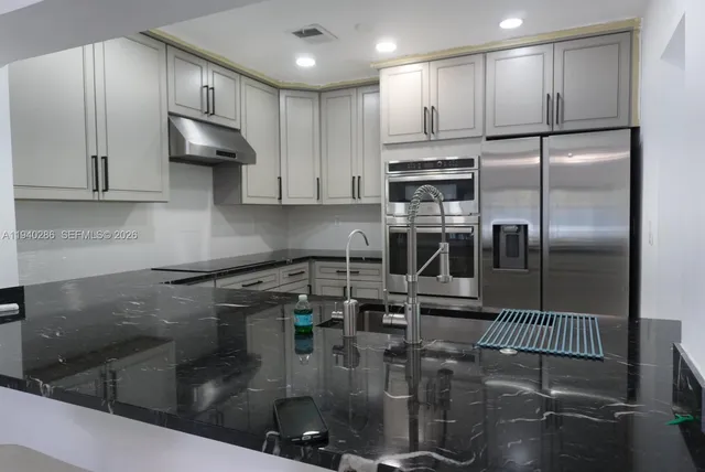 a kitchen with stainless steel appliances granite countertop a refrigerator a sink a stove and white cabinets
