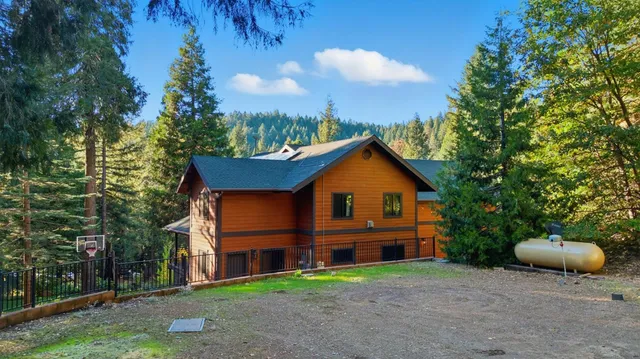 a view of a brick house with a yard plants and large tree