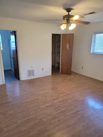 a view of an empty room with wooden floor and a ceiling fan