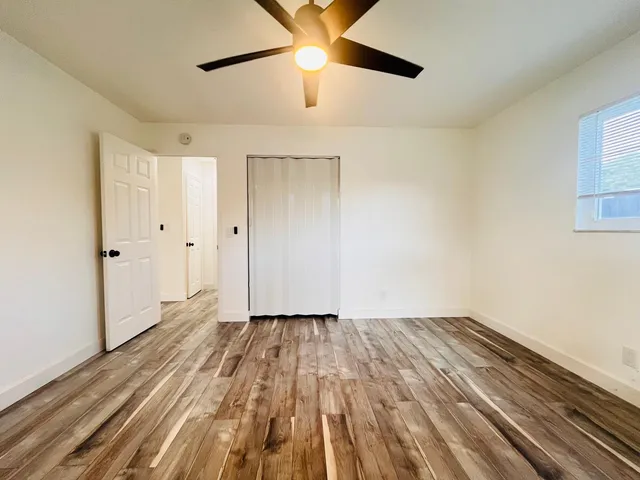 a view of an empty room with wooden floor and a ceiling fan