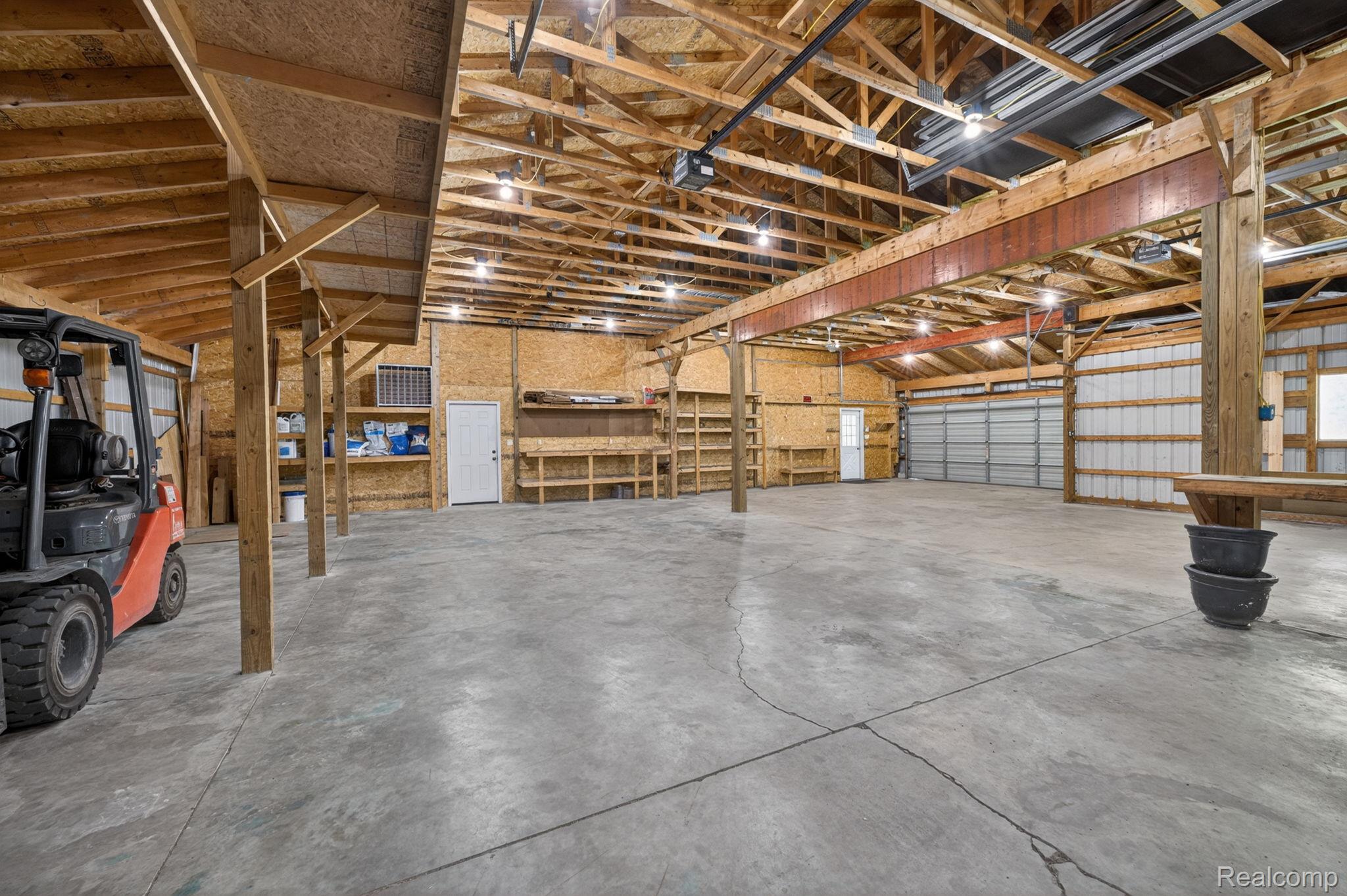 9353 Hill Road Swartz Creek, MI 48473 - Photo 77 of 98 Spacious open interior featuring a concrete floor, exposed wooden beam ceiling, two overhead garage doors, and built-in shelving