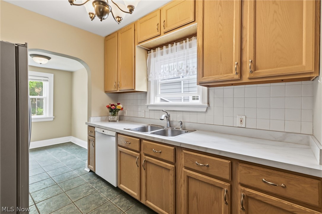 3511 Northcliffe Road Cleveland, OH 44118 - Photo 13 of 46 Galley kitchen featuring wood cabinetry with brass hardware, white subway tile backsplash, laminate countertops, stainless steel sink with faucet, and tile flooring