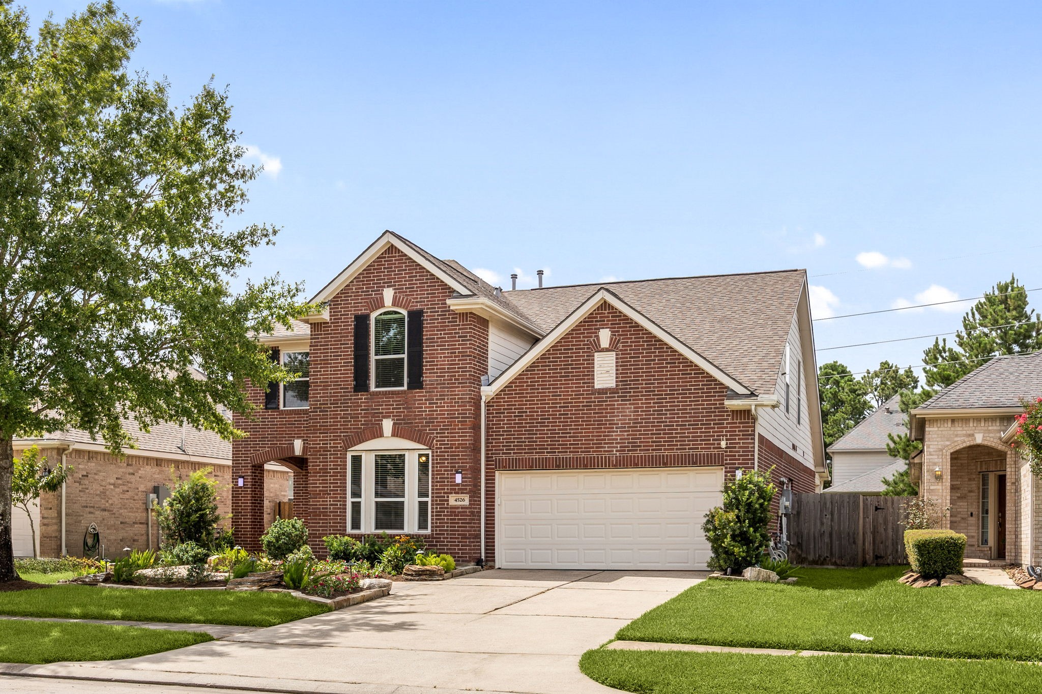 4526 Countrypines Drive Spring, TX 77388 - Photo 2 of 38 Timeless red brick exterior showcasing a grand gabled roofline, elegant shuttered windows, and a wide concrete driveway. Nestled on a beautifully landscaped lot with mature trees and a pristine green lawn.