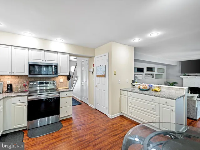 a kitchen with stainless steel appliances a stove top oven a sink a refrigerator white cabinets and wooden floor