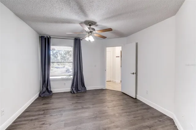 an empty room with wooden floor chandelier fan and windows