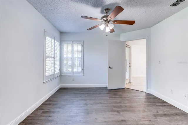 an empty room with wooden floor fan and windows