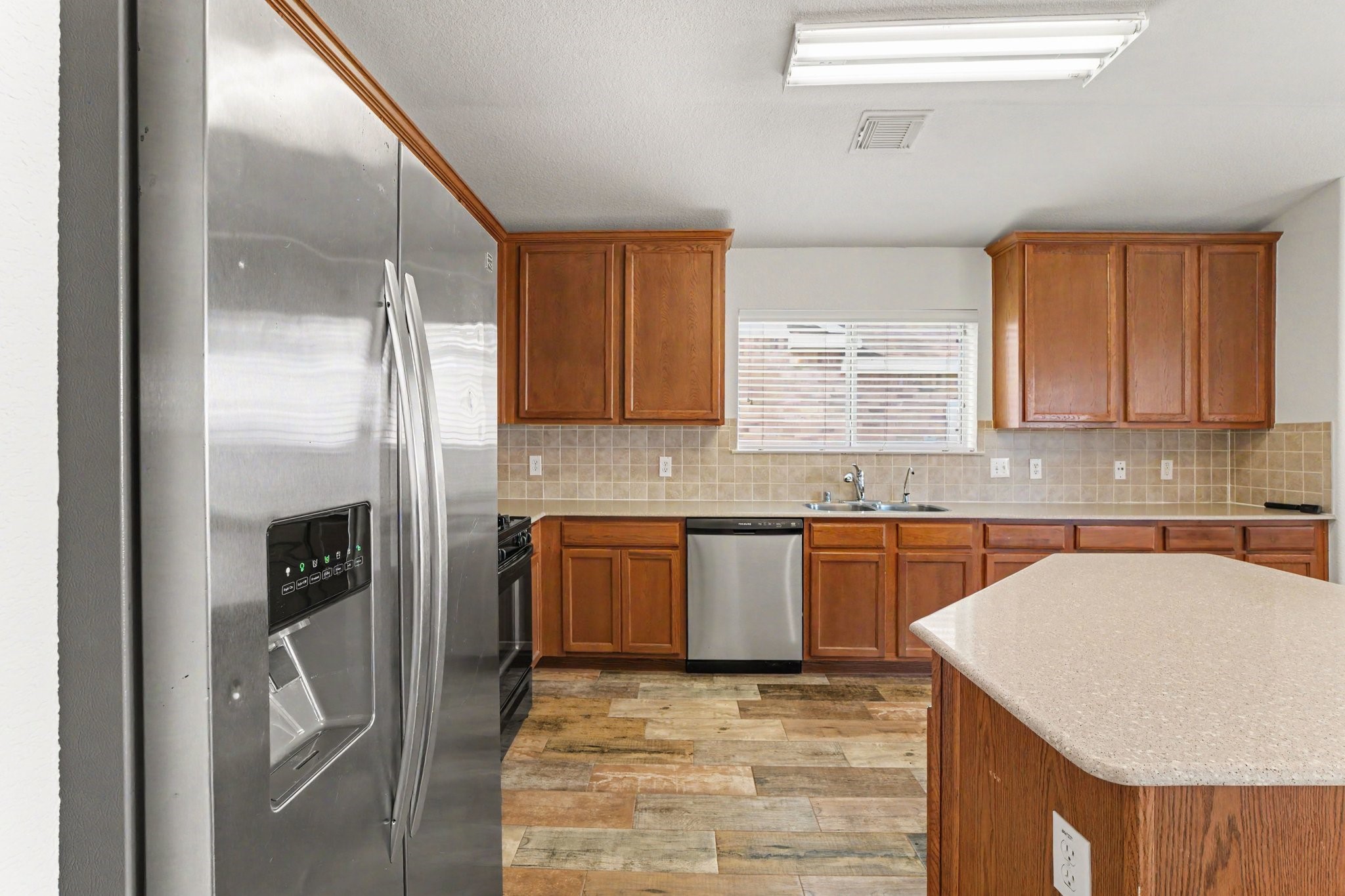 21427 Blooming Rock Lane Spring, TX 77379 - Photo 13 of 32 Modern kitchen with stainless steel appliances, spacious wooden cabinets, and a central island. It features a tiled backsplash, ample counter space, and natural light from a large window.