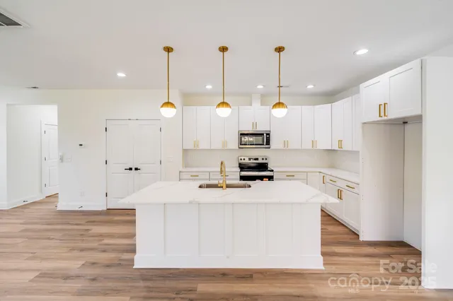 a large kitchen with stainless steel appliances kitchen island granite countertop a refrigerator a stove and white cabinets with wooden floor