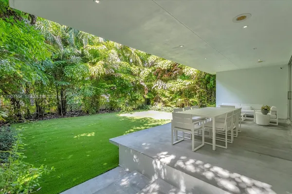 a view of a patio with couches table and chairs under an umbrella with large trees