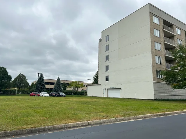 a view of a apartment with a big yard and large trees