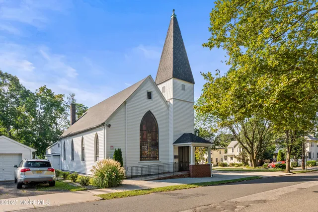 a view of a white house next to a road and large trees