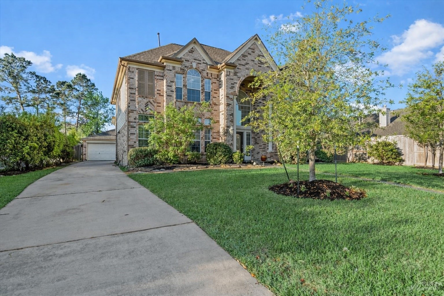 6507 Quiet Pointe Drive Spring, TX 77389 - Photo 26 of 45 This photo shows a two-story brick house with large, arched windows and a well-maintained front yard. The driveway leads to a detached garage, surrounded by trees and greenery, offering a welcoming curb appeal.