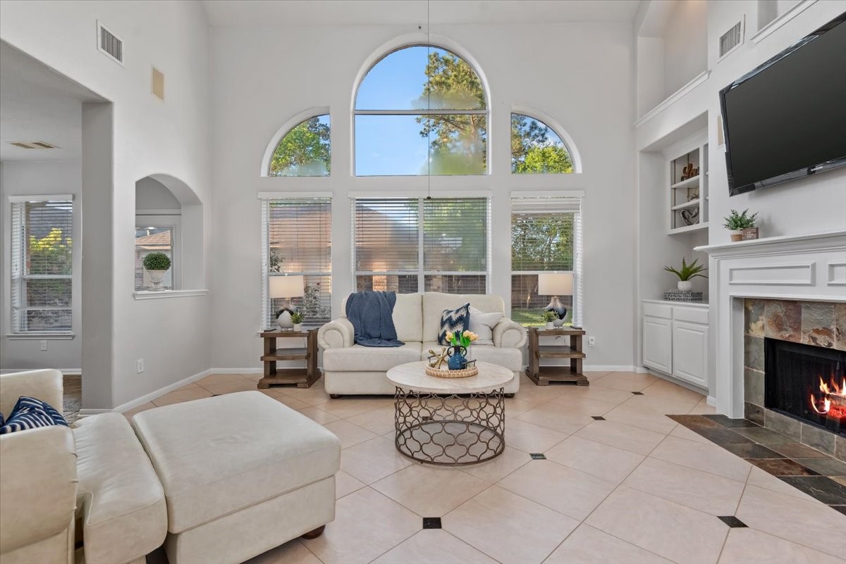 6507 Quiet Pointe Drive Spring, TX 77389 - Photo 4 of 45 This inviting living room features high ceilings with large arched windows that let in plenty of natural light. It has a cozy fireplace, built-in shelving, and stylish tile flooring. The neutral color palette and open layout create a bright and welcoming atmosphere.