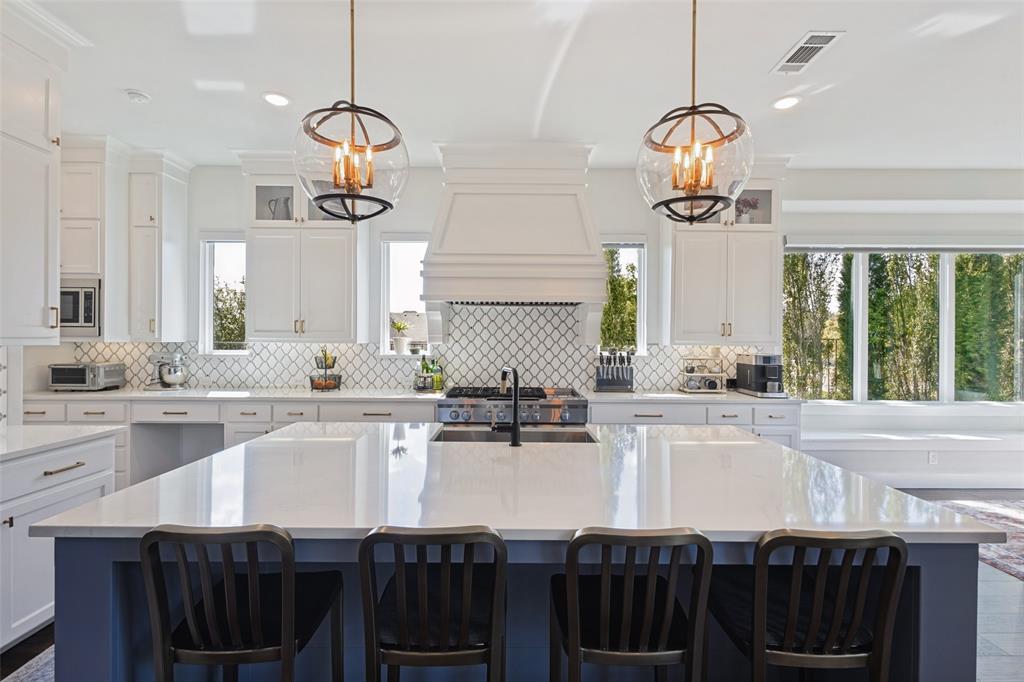 15018 Crape Myrtle Road Frisco, TX 75035 - Photo 10 of 40 Spacious kitchen with a large island, white cabinetry, integrated range hood, patterned tile backsplash, and oversized windows