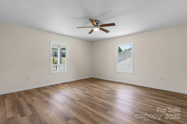 an empty room with wooden floor ceiling fan and windows