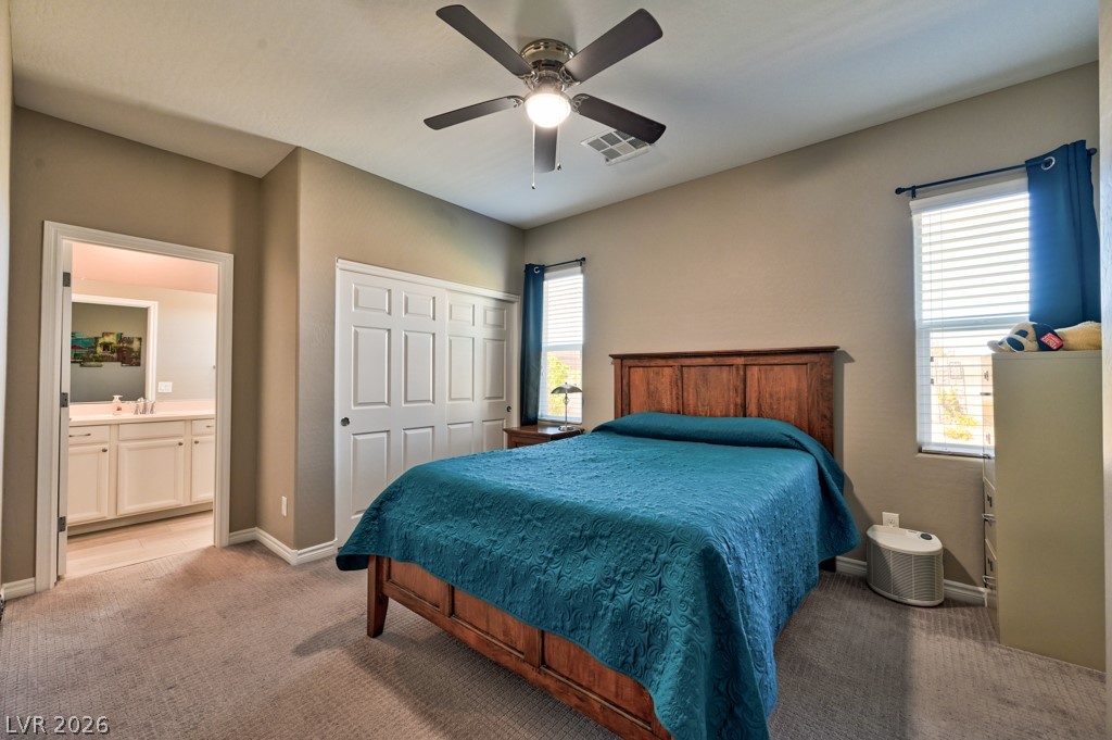 1054 Langston Ranch Avenue Henderson, NV 89002 - Photo 30 of 82 CASITA Bedroom featuring light carpet, a lighted ceiling fan, a closet, and connected bathroom. Windows for cheerful natural light.