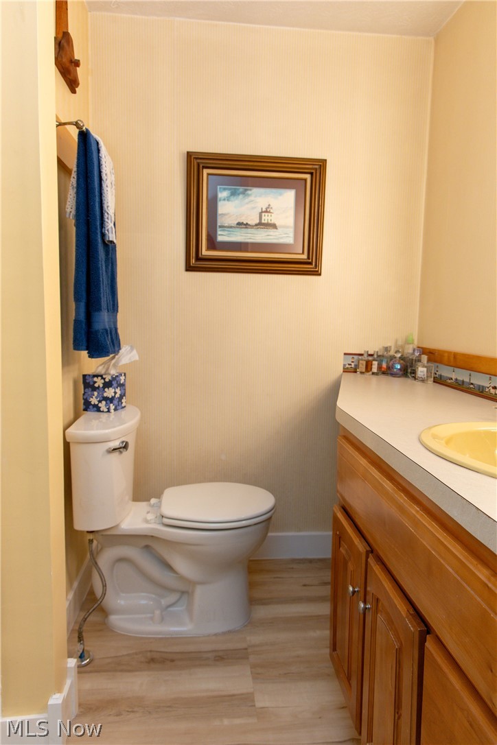 5467 Chapel Road Madison, OH 44057 - Photo 36 of 50 Bathroom featuring a white toilet, wood-finish flooring, a wood vanity with cabinet storage, a light-colored countertop, and a yellow drop-in sink