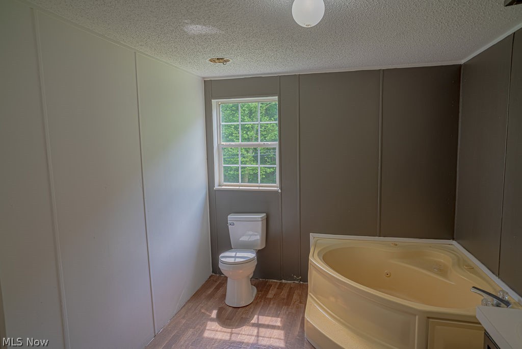 967 Buck Run Road Mineral Wells, WV 26150 - Photo 37 of 50 Bathroom featuring a corner jetted tub, a white toilet, and wood-finish flooring