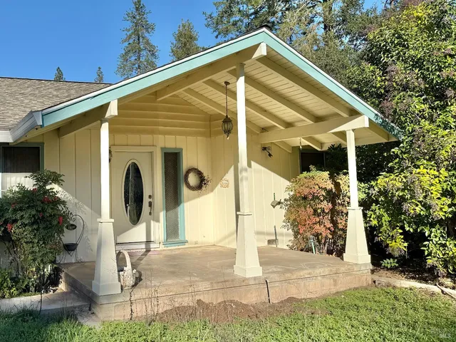 a view of a house with small yard plants and large tree