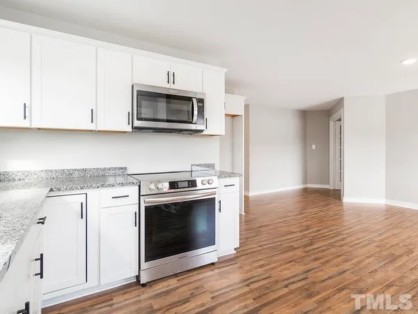 a kitchen with stainless steel appliances granite countertop a stove top oven a sink and white cabinets