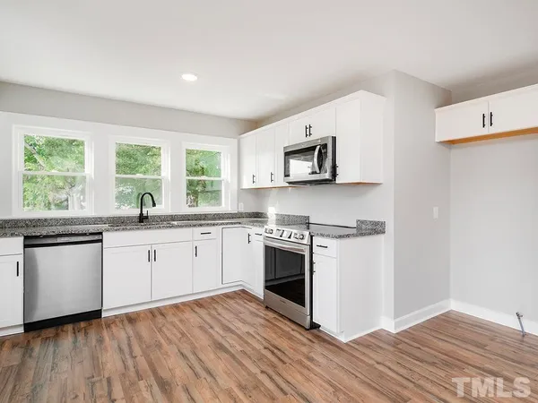 a kitchen with stainless steel appliances granite countertop a stove top oven a sink dishwasher and a refrigerator with wooden floor