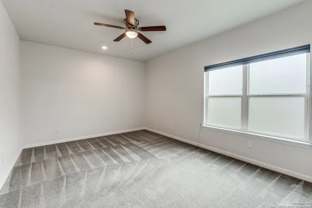 an empty room with chandelier fan and windows