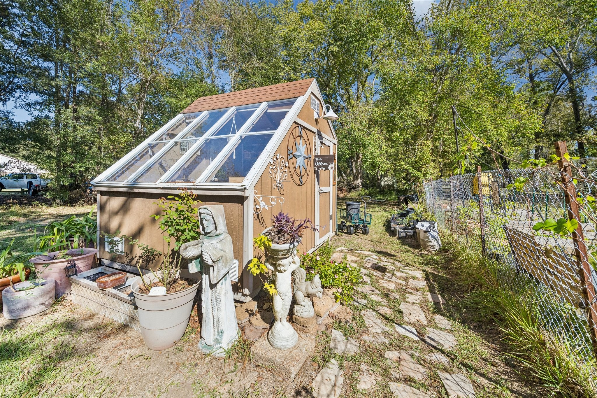 6 B Davidson Lane Huffman, TX 77336 - Photo 19 of 20 This photo showcases a charming greenhouse with large windows for natural light, surrounded by lush greenery with a stone path leading to it, offering a serene backyard retreat.