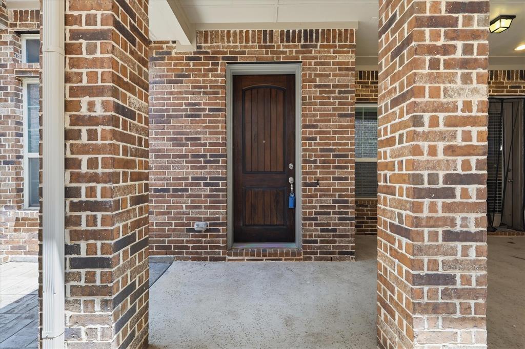 768 Huntingdon Street Coppell, TX 75019 - Photo 34 of 37 Covered front porch area with rich brickwork, a stained wood front door, and protected entryway that feels warm and inviting.