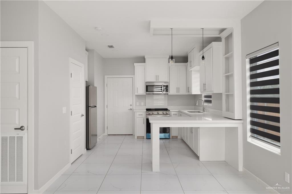 904 Deluxe Street Alamo, TX 78516 - Photo 2 of 11 Kitchen featuring open shelves, appliances with stainless steel finishes, decorative light fixtures, white cabinets, and a peninsula
