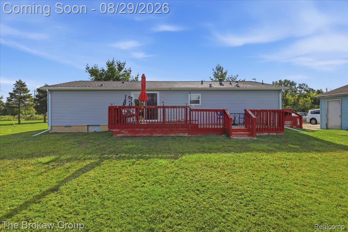 Expansive backyard featuring a manicured lawn, a multi-tiered wood deck, vinyl siding, and a detached garage