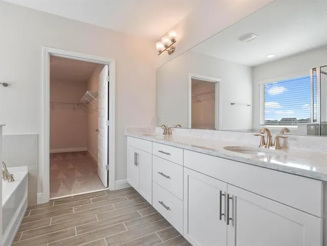 a spacious bathroom with a double vanity sink a mirror a bathtub and next to a window