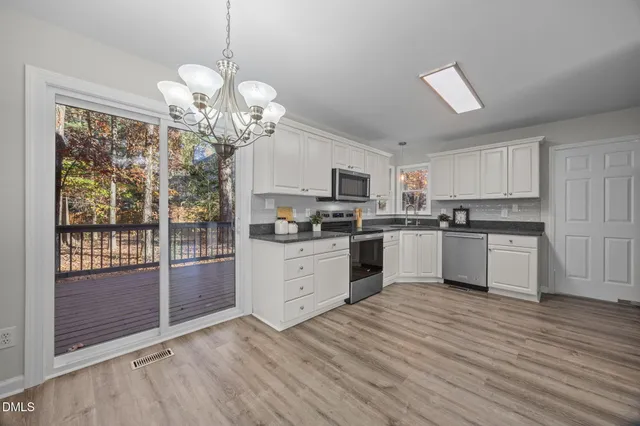 a kitchen with granite countertop a stove a sink dishwasher a refrigerator and white cabinets with wooden floor