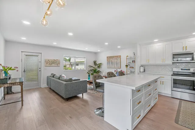a large white kitchen with a large counter top stainless steel appliances and wooden floor