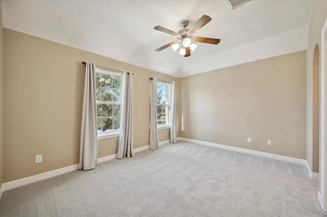 an empty room with chandelier fan and windows