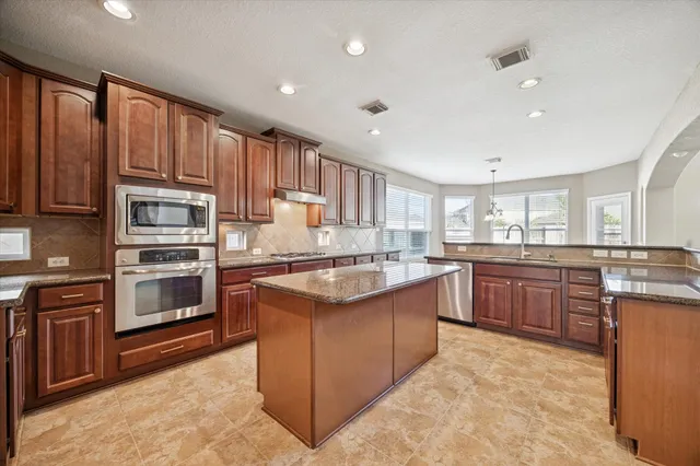 a kitchen with kitchen island granite countertop wooden cabinets stainless steel appliances and a counter space