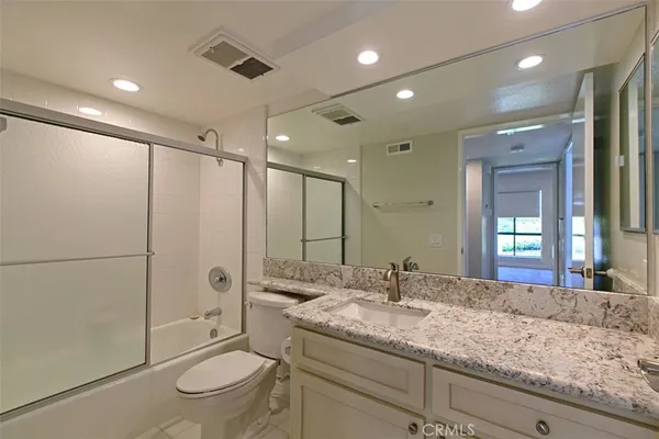 a bathroom with a granite countertop sink a toilet a mirror and shower