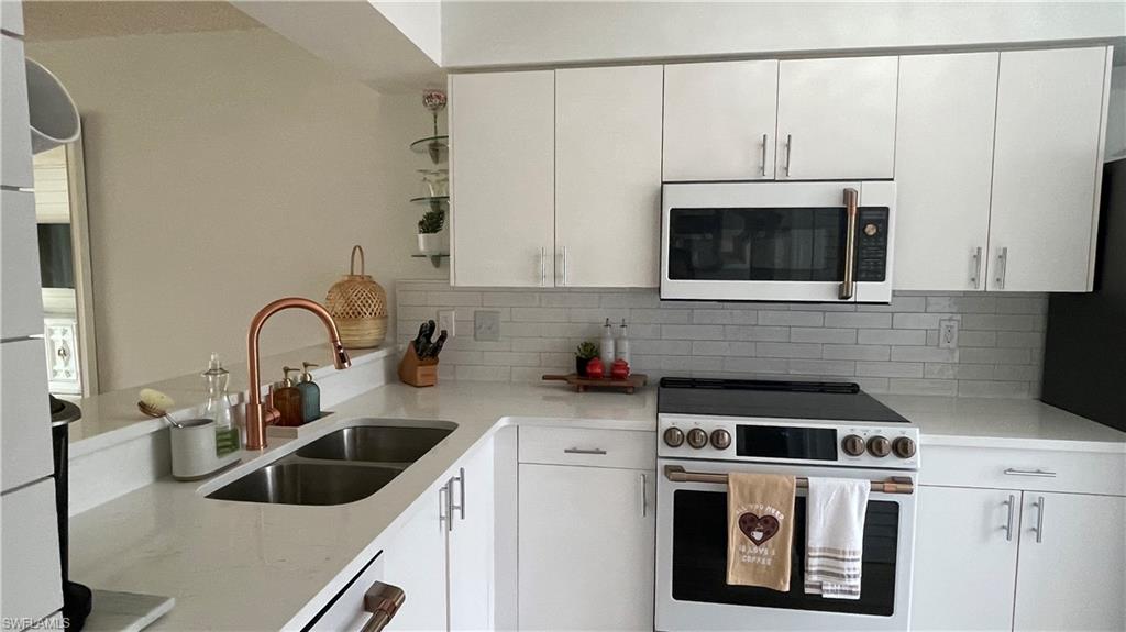 267 Quail Forest Boulevard, Unit 111 Naples, FL 34105 - Photo 11 of 41 a kitchen with white cabinets a sink and a stove with wooden floor