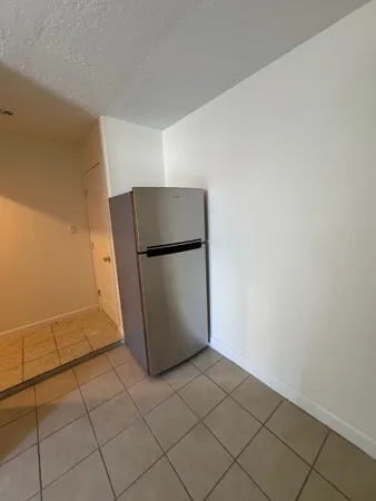 a view of a refrigerator in kitchen and an empty room