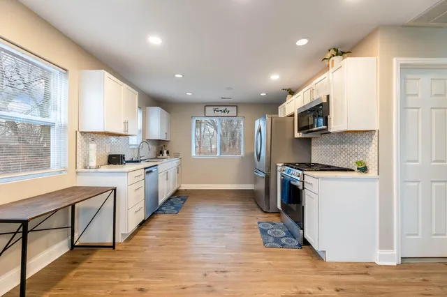 a kitchen with stainless steel appliances granite countertop a refrigerator a sink dishwasher a oven with white cabinets and wooden floor