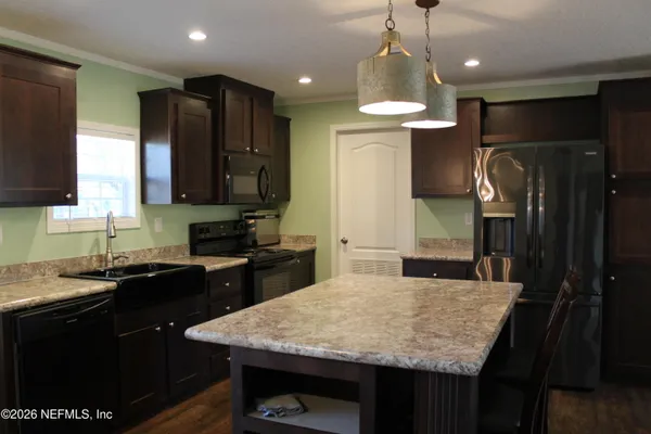 a kitchen with stainless steel appliances kitchen island granite countertop a sink dishwasher a refrigerator with wooden cabinets and floor