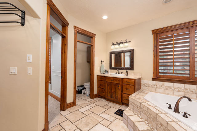 687 South 2080th Street East Springville, UT 84663 - Photo 22 of 149 Bathroom featuring wood-finish cabinetry, a single vanity with a light-toned countertop, and a built-in tub with tile surround