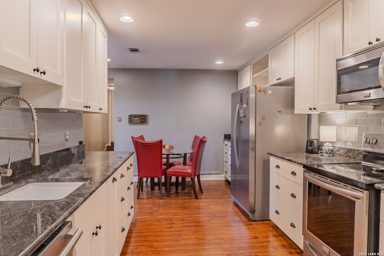 8942 Willmon Way Windcrest, TX 78239 - Photo 17 of 44 a kitchen with stainless steel appliances granite countertop a stove top oven a sink dishwasher a dining table and chairs with wooden floor